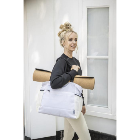Sac cabas blanc porté à l’épaule par une personne vêtue de clair, avec tapis de yoga fixé sur le dessus. Aucune personnalisation