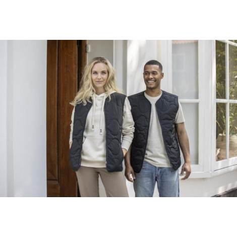 Gilet matelassé noir porté par une femme et un homme, présenté en extérieur. Aucune personnalisation visible. Gilet matelassé noir porté par une femme et un homme, présenté en extérieur. Aucune personnalisation visible.