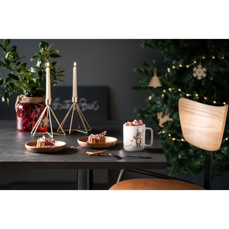 Scène de table décorée pour les fêtes, tasse blanche remplie de chocolat chaud posée à côté d’un sapin illuminé, sans marquage v