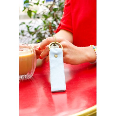 Porte clé bleu clair tenue dans une main avec tasse de café posée à côté