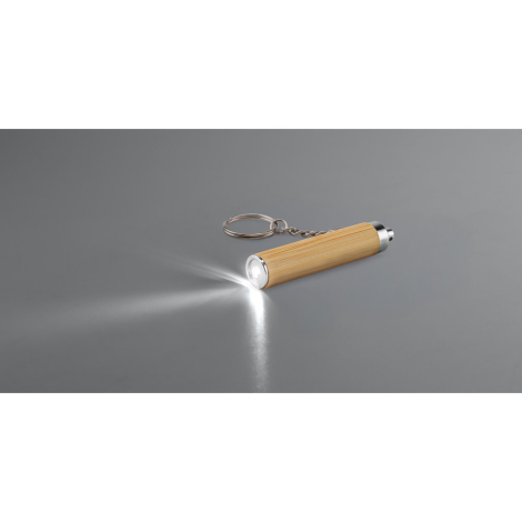 Lampe LED allumée fixée au porte-clés, posée sur une surface grise, sans marquage visible.