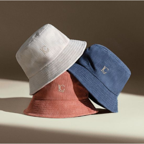 Trois bobs en velours côtelé de couleurs beige, terracotta et bleu, présentés empilés les uns sur les autres. Sans marquage appa