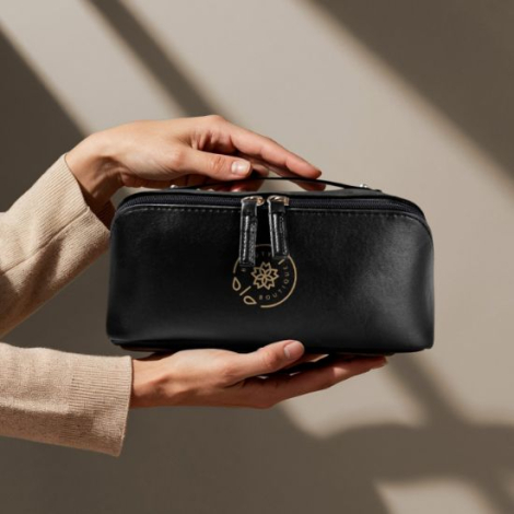 Trousse noire tenue entre les mains d’une femme, illustrant la texture lisse et le format généreux, avec marquage visible sur la