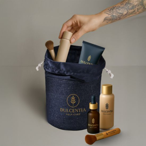 Trousse en toile denim bleue ouverte contenant des accessoires de soin et de beauté, avec un marquage visible sur la face avant.