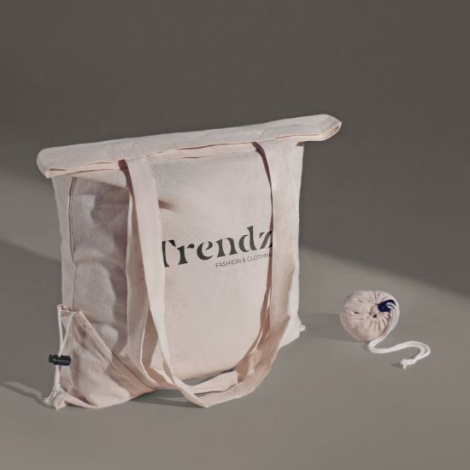 Sac beige déplié posé sur fond uni, accompagné de sa version pliée en pochette ronde, présentant un marquage visible sur la face