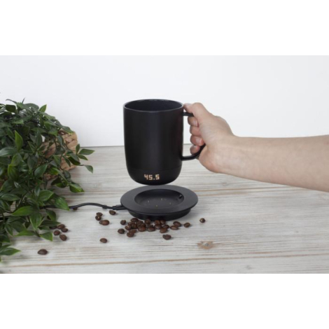 Mug noir tenu dans une main, positionné au-dessus de son support de charge, écran LED actif indiquant une température ; marquage