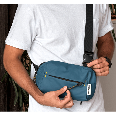 Vue portée montrant la sacoche bleue en bandoulière sur un homme, tenue à l’avant du corps, sans marquage apparent sur cette vue