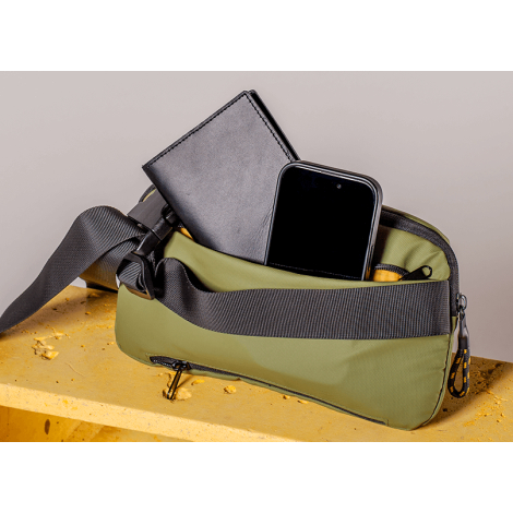 Vue rapprochée d’une version verte de la sacoche ouverte, révélant un téléphone et un portefeuille dans le compartiment principa