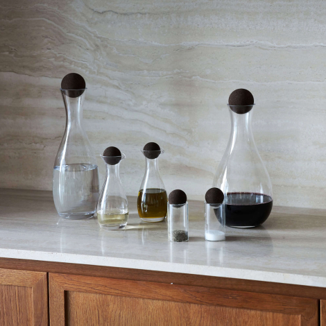 Carafe en verre partiellement remplie présentée dans un intérieur aux côtés d’autres récipients assortis fermés par un bouchon s