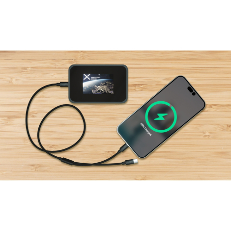 Mise en situation sur surface en bois montrant la powerbank reliée par un câble à un smartphone, écran LCD allumé affichant une 