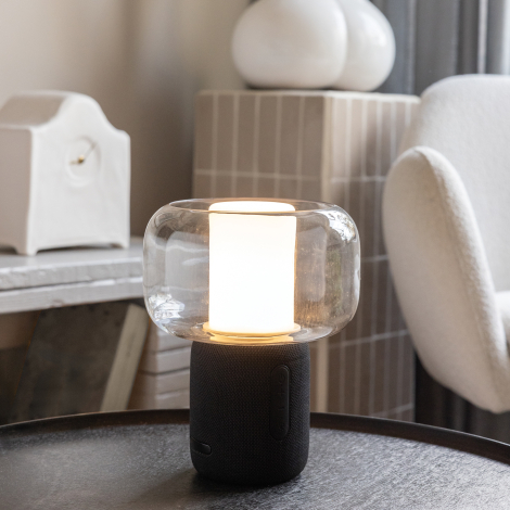 Lampe allumée placée sur une table en environnement intérieur, diffuseur en verre visible et socle noir avec boutons de commande