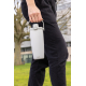 Mug isotherme blanc porté à la main par une personne en extérieur, transporté par la poignée supérieure, sans bandoulière visibl