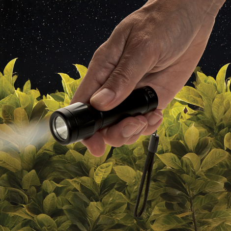 Lampe torche tenue à la main en environnement extérieur sombre, faisceau lumineux allumé dirigé vers l’avant et dragonne visible