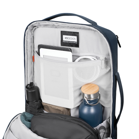 Sac à dos ouvert sur fond blanc, intérieur organisé avec compartiments, poches filet et objets rangés visibles, étiquette intéri