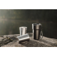 Scène extérieure montrant une tasse de rangement noire avec anse et cordon, accompagnée de trois tasses en acier inoxydable posé Scène extérieure montrant une tasse de rangement noire avec anse et cordon, accompagnée de trois tasses en acier inoxydable posé