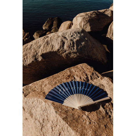 Éventail ouvert posé sur des rochers en extérieur, avec toile bleu foncé et claire tendue sur une structure en bambou, la poigné
