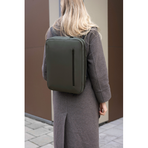 Sac porté sur le dos par une femme en environnement urbain, de couleur vert foncé, avec fermeture zippée verticale visible sur l