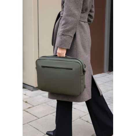 Sac porté à la main par une femme en environnement urbain, de couleur vert foncé, avec poignée supérieure et poche zippée horizo