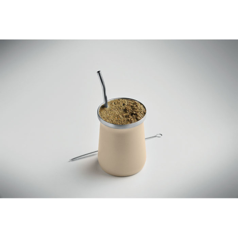 Tasse à yerba maté présentée debout sur surface claire remplie de yerba avec paille insérée et brosse de nettoyage posée à côté,
