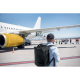 Scène de vie montrant un homme portant un sac à dos cabine sur un tarmac d’aéroport face à un avion, sans marquage visible sur l Scène de vie montrant un homme portant un sac à dos cabine sur un tarmac d’aéroport face à un avion, sans marquage visible sur l