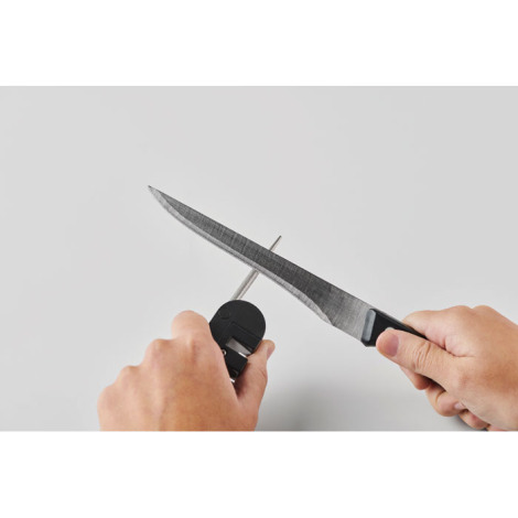 Scène d’utilisation montrant un aiguiseur de poche tenu à deux mains avec un couteau appliqué sur la tige d’aiguisage, sans marq