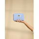 Trousse rectangulaire de couleur bleu clair, vue de face et tenue dans une main sur fond uni, fermeture zippée située sur le côt Trousse rectangulaire de couleur bleu clair, vue de face et tenue dans une main sur fond uni, fermeture zippée située sur le côt