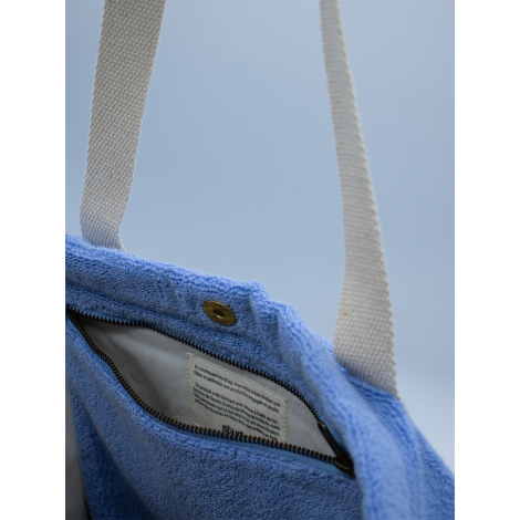 Sac de plage publicitaire en coton bio éponge bleu, vue rapprochée de l’ouverture et des anses, sans personnalisation visible.