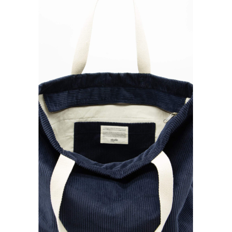 Vue plongeante de l’intérieur d’un sac cabas bleu foncé montrant ouverture zippée, doublure claire et étiquette cousue, sans mar