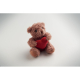 Ours en peluche présenté en légère perspective sur fond clair, assis et tenant un cœur rouge, avec détails brodés du visage visi