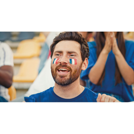 Homme dans les tribunes d’un stade avec maquillage appliqué sur les joues, produit utilisé sans marquage visible apparent.