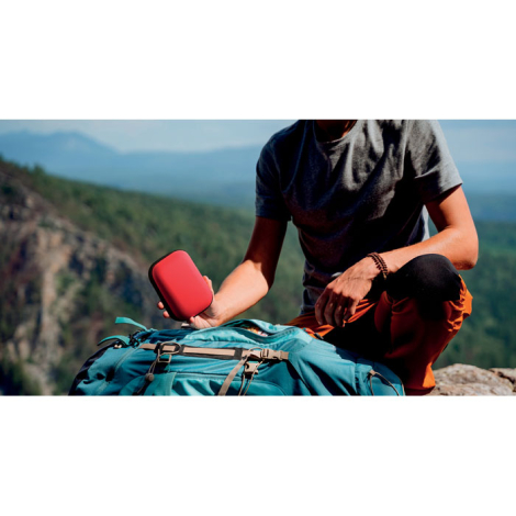 Trousse de premiers secours rouge tenue à la main en contexte extérieur au-dessus d’un sac à dos, avec personnalisation visible 