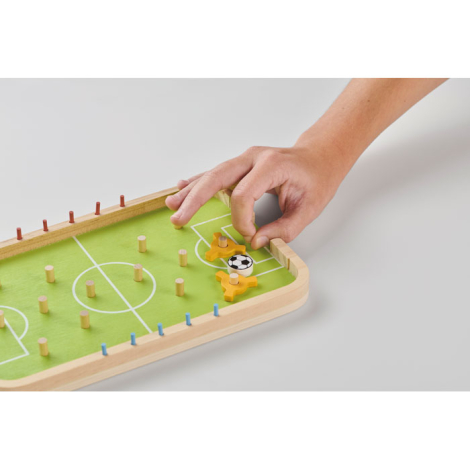 Présenté en situation sur fond clair, le plateau de football de table est manipulé à la main avec pièces mobiles visibles sur le