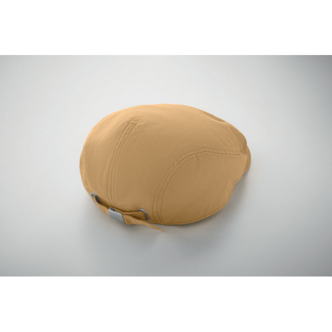 Présentée de dos, une casquette plate beige montre la fermeture arrière réglable avec boucle métallique et les œillets, sans mar