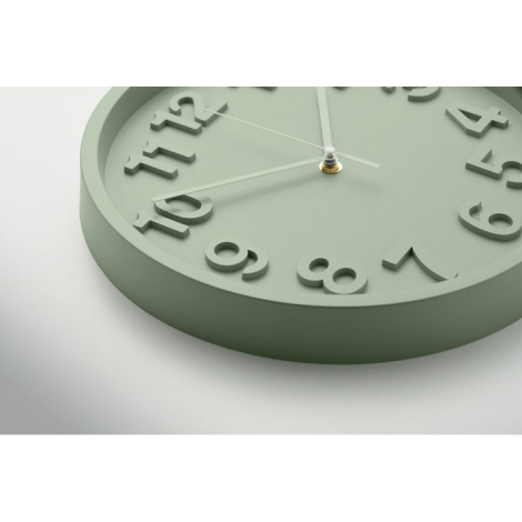 En gros plan et en légère perspective, une horloge murale ronde vert clair met en évidence les chiffres en relief et les aiguill