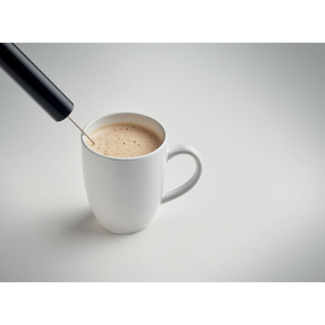 Mousseur à lait en situation d’utilisation au-dessus d’une tasse contenant une boisson mousseuse, tige et fouet plongés dans le 