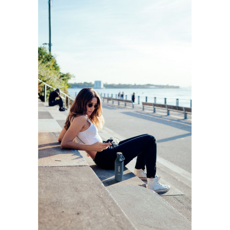 Bouteille à simple paroi présentée en situation extérieure posée au sol à proximité d’une personne assise, personnalisation visi