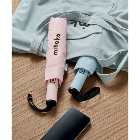 Deux parapluies pliés sur un sac en tissu posé sur une surface en bois, l’un rose et l’autre bleu clair, rangés dans leurs houss