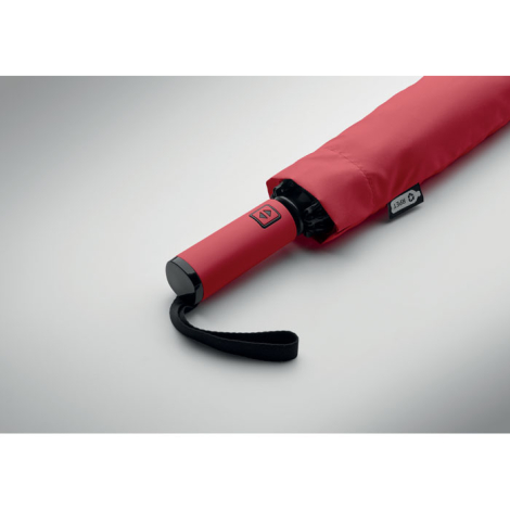 Gros plan sur la poignée d’un parapluie plié rouge avec dragonne noire sur fond clair, avec personnalisation visible sur la poig