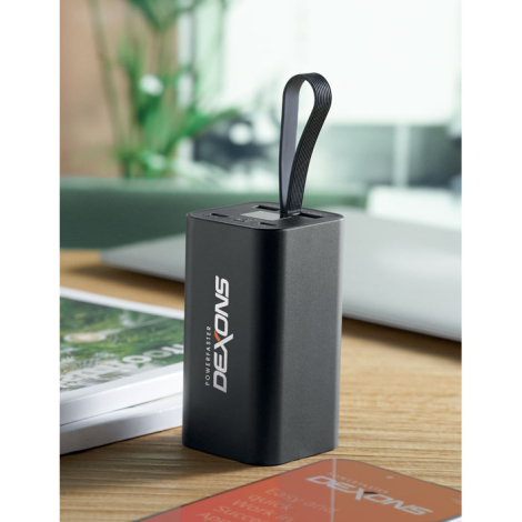 Powerbank posée sur un bureau en vue de trois-quarts avec personnalisation blanche visible en impression verticale sur la face a