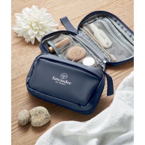 Trousse de toilette bleue ouverte posée sur une surface avec compartiments intérieurs en filet et accessoires rangés, personnali