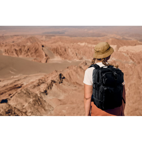 Sac à dos porté par une personne en extérieur vu de dos dans un paysage désertique, sans personnalisation visible.