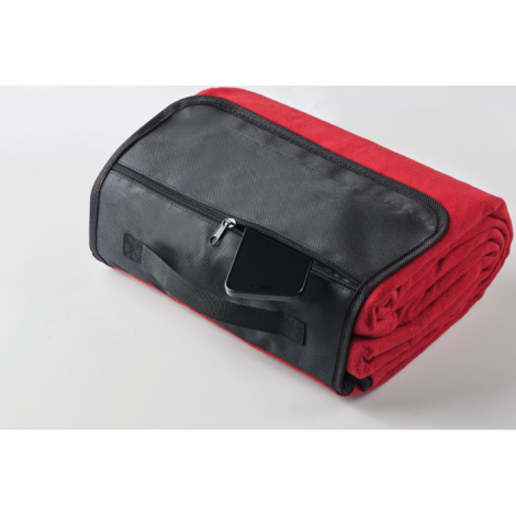 Couverture rouge roulée maintenue par rabat noir avec poche zippée, présentée en perspective sans marquage visible.