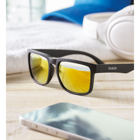 Lunettes de soleil noires avec verres miroirs dorés posées sur une surface en bois avec casque et smartphone en arrière-plan, ma