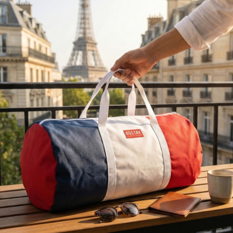 Sac polochon tricolore bleu, blanc et rouge posé sur une table en extérieur, anses blanches et fermeture zippée visibles, marqua