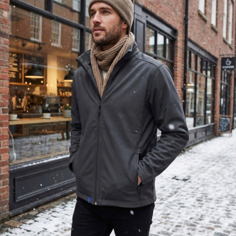 Veste softshell gris foncé portée par un modèle en extérieur dans une rue pavée, sans personnalisation visible sur le vêtement.