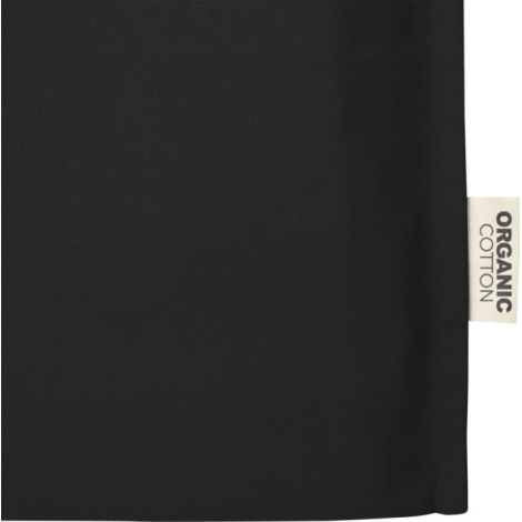 Gros plan sur la partie inférieure d’un sac shopping noir avec étiquette textile latérale mentionnant la composition, sans marqu