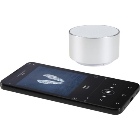Enceinte cylindrique argentée positionnée à côté d’un smartphone affichant une interface musicale, sans personnalisation visible
