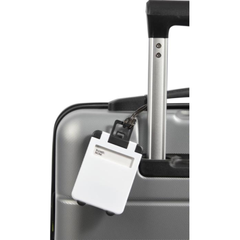 Étiquette à bagage blanche attachée à la poignée télescopique d’une valise grise, maintenue par une boucle souple et un support 
