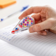 Correcteur Tipp-Ex Mini Pocket Mouse tenu en main en utilisation sur un cahier, avec capot transparent et marquage apparent sur 