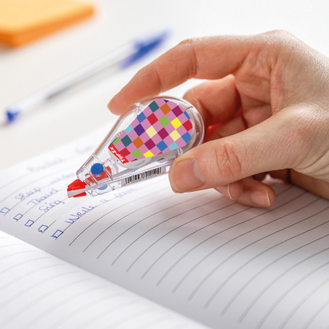 Correcteur Tipp-Ex Mini Pocket Mouse tenu en main en utilisation sur un cahier, avec capot transparent et marquage apparent sur 